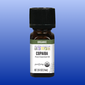 Bottle of Aura Cacia Copaiba Organic Essential Oil 0.25 oz with purifying properties on blue background