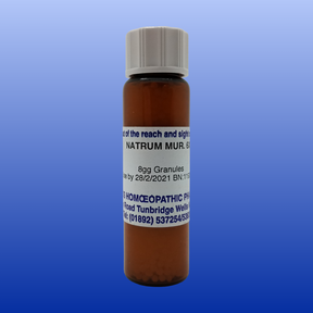Brown glass bottle of Nat Mur 6X lactose-free cell salt granules with white label and gray cap on blue background