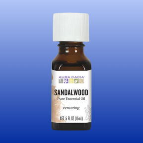 Bottle of Aura Cacia sandalwood pure essential oil 0.5 fl oz with white cap on blue background