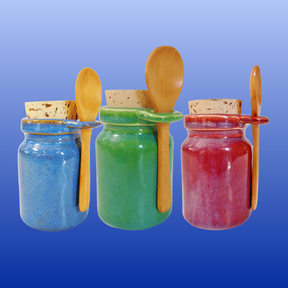 Three colorful ceramic neti salt storage jars with wooden spoons and cork lids on a blue background