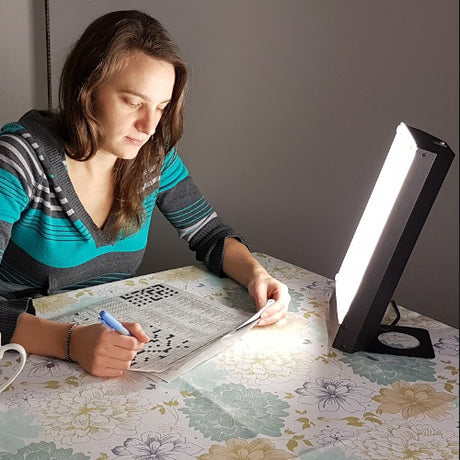 Woman using TRAVelite Desk Lamp for bright light while doing a crossword puzzle at a table indoors